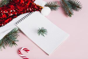 Blank notebook, santa claus hat and fir branches on pink background photo