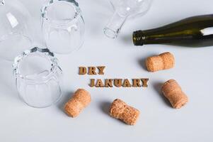 Overturned glasses, empty bottles, corks and text dry january on gray background photo