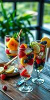 Colorful fruit cocktails served in tall glasses with ice on a wooden table, surrounded by greenery photo