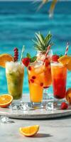 Colorful tropical cocktails displayed on a marble table by the beach with clear turquoise water in the background photo