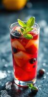 Refreshing fruit cocktail with strawberries, blueberries, and mint served in a clear glass on a dark surface photo