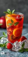 Refreshing fruit beverage garnished with mint and surrounded by fresh strawberries and ice cubes in a stylish glass photo