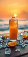Refreshing cocktail sits on a table with ice and orange slices as the sun sets over the ocean photo