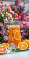 Refreshing orange drink served in a pitcher with fresh fruits and ice beside colorful flowers in a garden setting photo