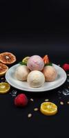 Colorful ice cream scoops served on a plate with fresh fruit and ice on a dark background photo