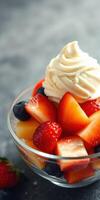 Fresh fruit salad topped with whipped cream served in a glass bowl on a textured gray background photo
