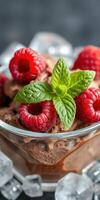 Delicious chocolate mousse topped with fresh raspberries and mint leaves served in a clear bowl photo