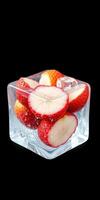 Fresh strawberries frozen in ice cube with a clear edge and bubbles highlighting the fruit's vibrant color photo