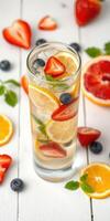 Refreshing fruit-infused beverage with citrus, berries, and ice in a tall glass on a white wooden table photo