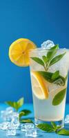 Refreshing lemon mint drink with ice served in a clear glass against a vibrant blue background photo