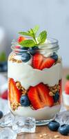 Delicious layered yogurt parfait with strawberries, blueberries, and granola in a glass jar on a wooden countertop photo