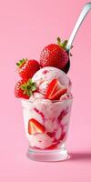 Fresh strawberry ice cream served in a clear glass bowl with whole strawberries on top against a pink background photo