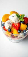 Colorful fruit salad topped with vanilla ice cream served in a clear glass bowl photo