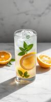 Refreshing lemon mint drink with ice in a tall glass on a marble surface photo