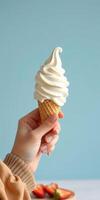 Delicious soft serve ice cream cone held by a hand against a light blue background photo