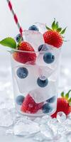 Refreshing summer drink with strawberries and blueberries in a glass with ice and a striped straw photo