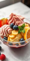 Colorful dessert bowl filled with assorted ice cream, fresh fruit, and mint leaves on a marble table photo