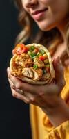 Woman enjoys a flavorful wrap filled with crispy chicken, fresh vegetables, and tomatoes in a cozy setting photo