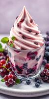 Delicious swirl of berry-flavored soft serve topped with fresh red and blue berries served in a clear glass cup photo