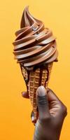 Hand holding a chocolate swirl ice cream cone against a vibrant yellow background photo