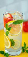 Refreshing lemonade infused with strawberries and mint garnished with lemon slices on a vibrant yellow background photo