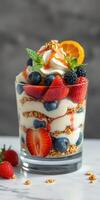 Delicious layered dessert with yogurt, berries, and granola in a glass served on a marble surface photo