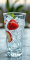 Refreshing drink with strawberries and ice in a clear glass on a marble surface during a sunny day photo