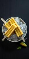 Cold summer treats with mango popsicles resting on ice in a bowl photo