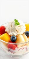 Delicious fruit salad with creamy ice cream topped with mint leaves in a clear bowl photo