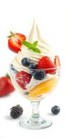 Decadent soft serve ice cream topped with fresh fruit and mint leaves in a clear glass dessert cup photo