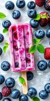 Colorful fruit popsicle surrounded by fresh blueberries and raspberries on ice photo