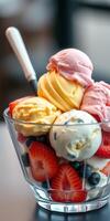 Colorful ice cream sundae topped with fresh strawberries and blueberries served in a glass dish on a table indoors photo
