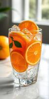 Refreshing orange beverage served in a clear glass filled with ice and citrus slices on a bright countertop photo