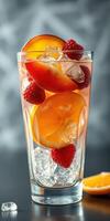 Refreshing fruit cocktail with ice and colorful berries in a tall glass on a dark background photo