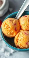 Bright and refreshing peach ice cream served in a teal bowl with a stainless steel spoon on a marble countertop photo