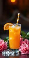 Refreshing orange drink served in a tall glass with a slice and a straw, surrounded by pink flowers photo