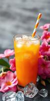 Refreshing orange drink garnished with tropical flowers and ice cubes on a sunny day photo