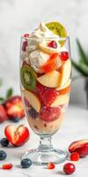 Colorful fruit parfait with cream topped with fresh fruits in a tall glass on a marble countertop photo