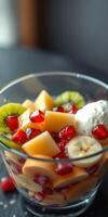 Fresh fruit salad with pomegranate and cream served in a clear glass bowl on a dark surface photo