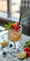 Refreshing fruit cocktail garnished with berries and mint placed on a marble table in a bright setting photo