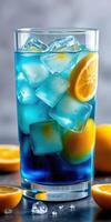Refreshing blue beverage with ice and lemon slices in a tall glass on a dark countertop photo