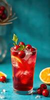 Refreshing berry and orange drink served in a tall glass with ice and mint leaf on a turquoise background photo