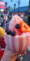 Colorful dessert topped with berries and banana enjoyed in a lively urban setting during the evening photo