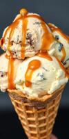 Ice cream cone topped with caramel drizzle and chocolate chunks at a dessert shop in the afternoon photo