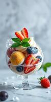 Colorful fruit salad in glass bowl topped with mint leaves and berries served on a marble countertop photo