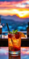 Refreshing cocktail with mint and fruit garnishes against a vibrant sunset backdrop in a rooftop bar photo