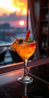 Bright tropical cocktail garnished with fruit placed on a bar during sunset at a rooftop lounge photo