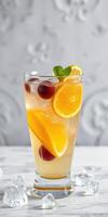 Refreshing fruit cocktail in a tall glass with ice and citrus garnish on a marble table photo