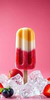 Colorful frozen treat on a stick surrounded by fresh strawberries and ice cubes in a pink setting during summer photo