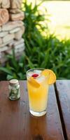 Refreshing summer cocktail served in a clear glass beside a small jar of herbs on a wooden table outdoors photo